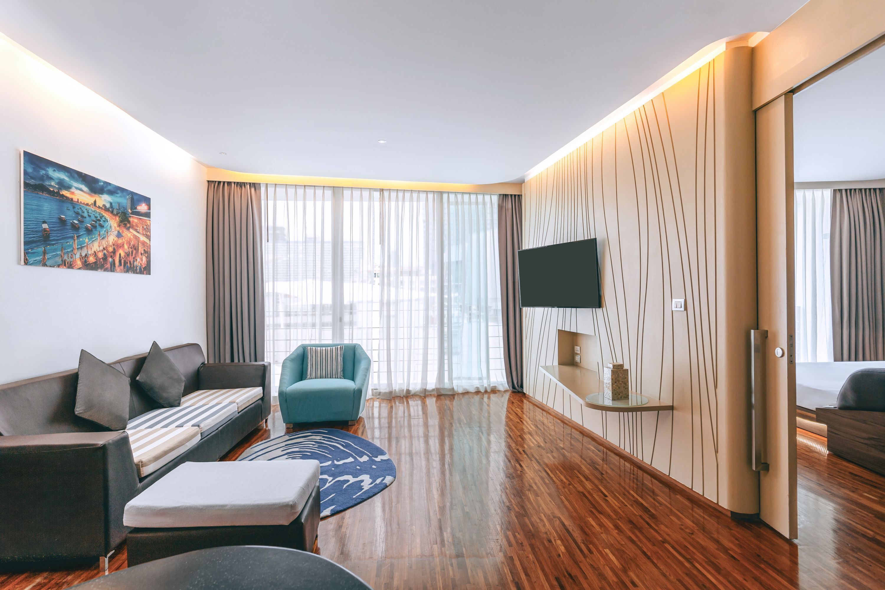 A modern hotel room with a sofa, armchair, and a flat-screen TV mounted on the wall.