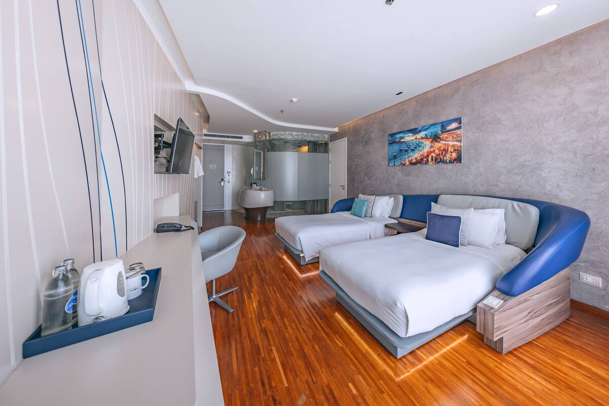Una habitación de hotel moderna con dos camas, un escritorio, una silla y un baño a la vista al fondo.