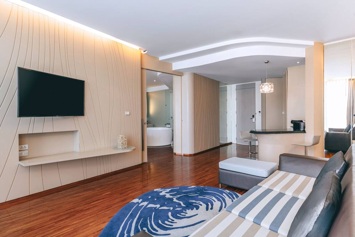 Una sala de estar moderna con un televisor de pantalla plana, un sofá, una mesa de centro y una alfombra estampada.