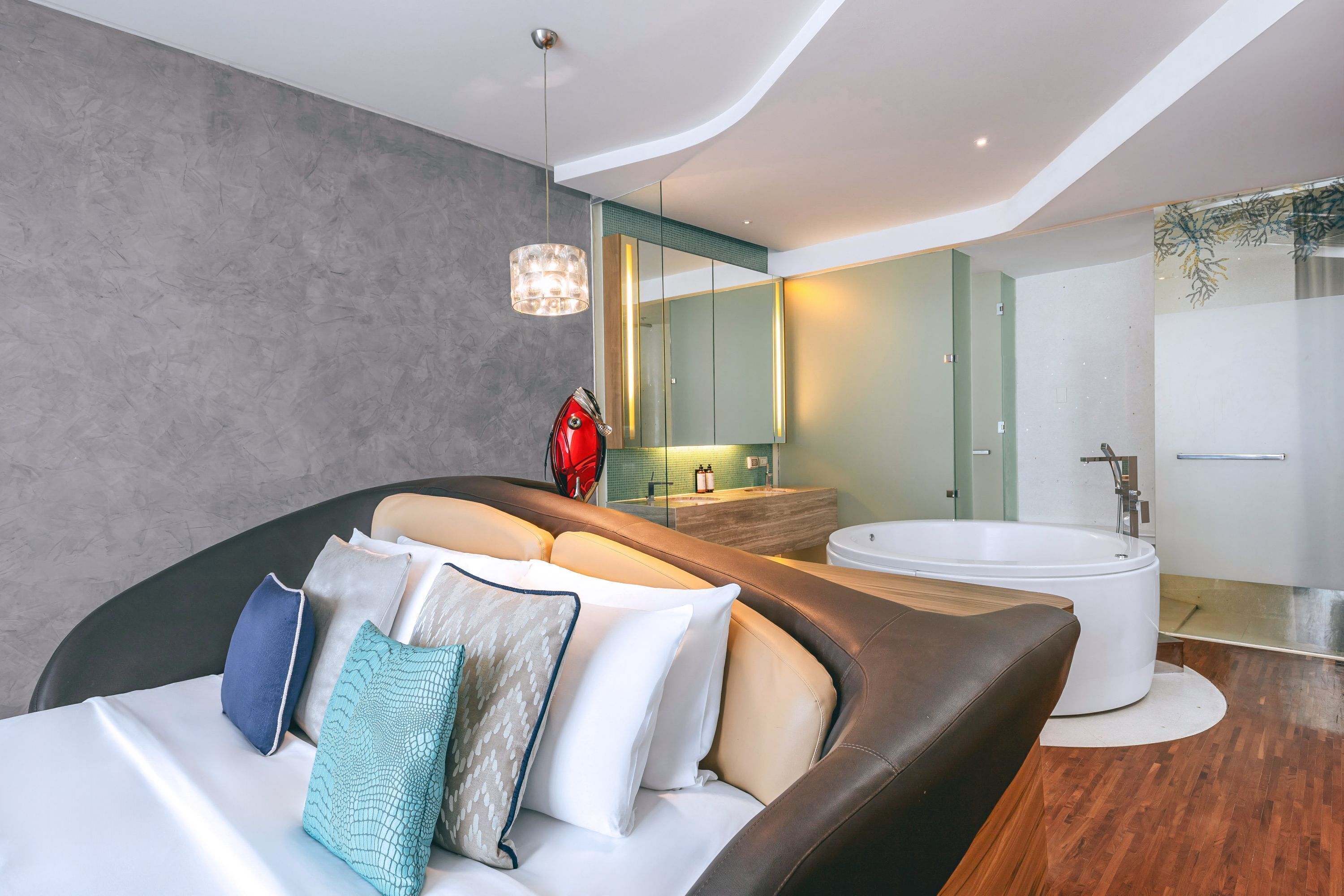 Une chambre à coucher moderne avec un lit aux lignes courbes, un grand miroir, une baignoire et un objet décoratif rouge.