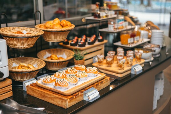A buffet with various food items including pastries, sandwiches, and beverages.