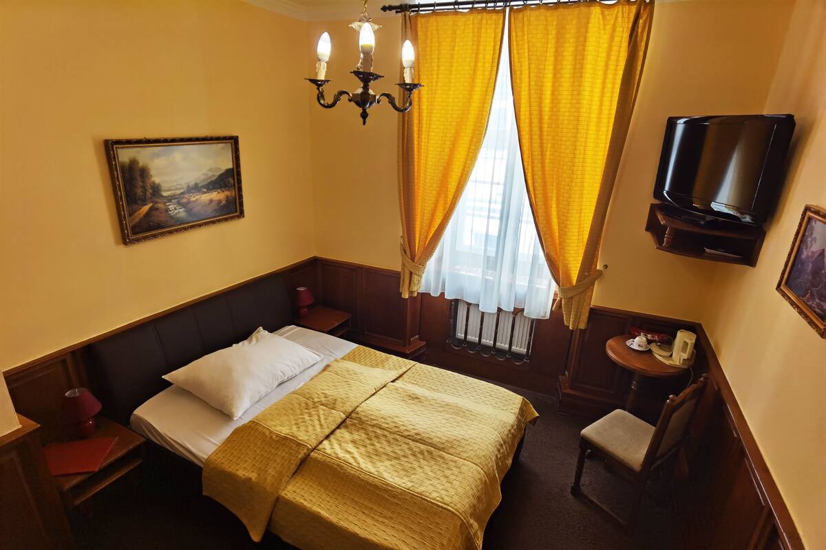A hotel room with a bed, a television, a chair, a small table, and a painting on the wall.