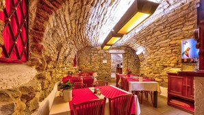 A stone-walled restaurant with red tablecloths and wooden chairs. Tables are arranged in a U-shape, and there is a wooden counter with a cash register. - Betlem Club Hotel (Prague)