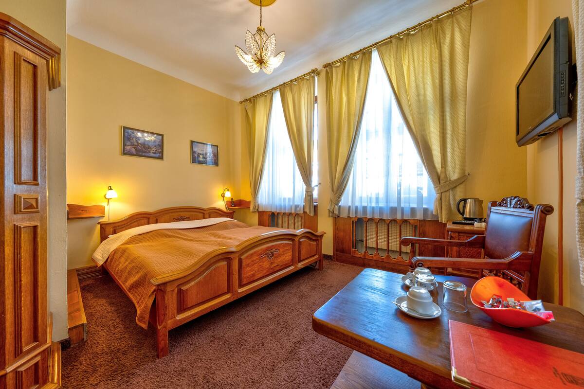 A hotel room with a wooden bed, a desk with a chair, a television, and a window with curtains.