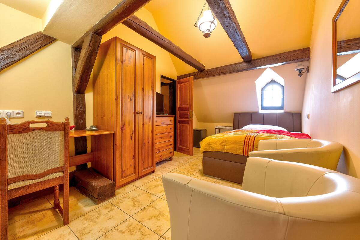 A bedroom with a wooden wardrobe, a desk, a bed with a yellow blanket, and a window with a view.
