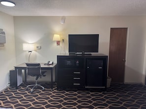 A hotel room with a desk, chair, lamp, TV, and a minibar. - Euclid Motel (Bay City)