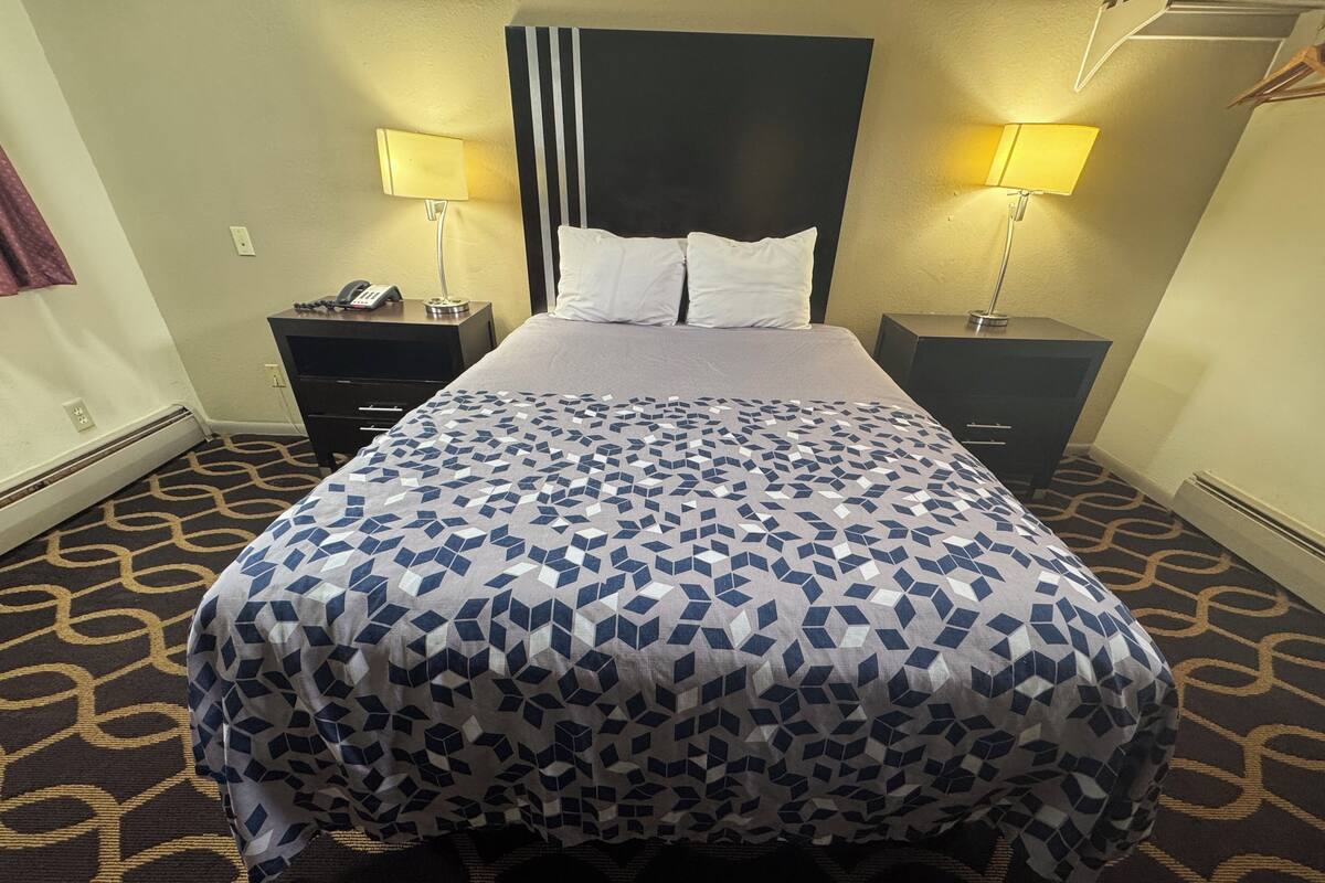 A hotel room with a bed, two bedside tables with lamps, a telephone, and a patterned carpet.