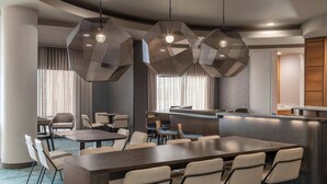 A modern hotel dining area with hexagonal pendant lights, a central dining table, and a bar counter. - SpringHill Suites Detroit Auburn Hills (Lake Orion)