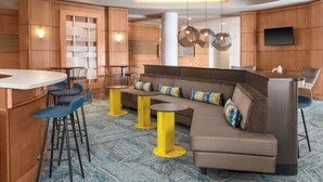 A modern hotel lobby with a curved seating area, bar stools, and a flat-screen TV mounted on the wall. - SpringHill Suites Detroit Auburn Hills (Lake Orion)
