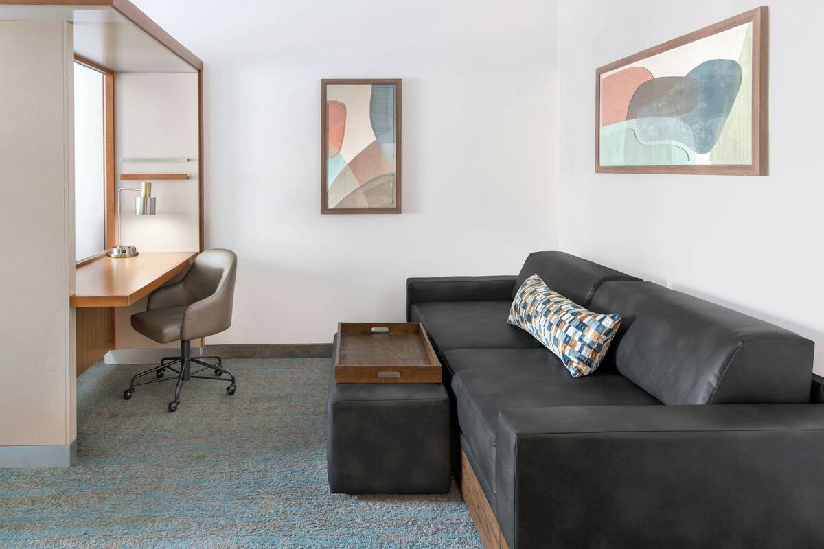 A modern room with a desk, chair, sofa, and artwork on the walls.