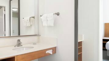 Un baño moderno con un lavamanos blanco, un espejo y dos toallas colgadas en barras para toallas.