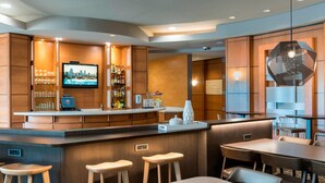 A modern bar area with a TV, bar counter, stools, and seating. - SpringHill Suites Detroit Auburn Hills (Lake Orion)