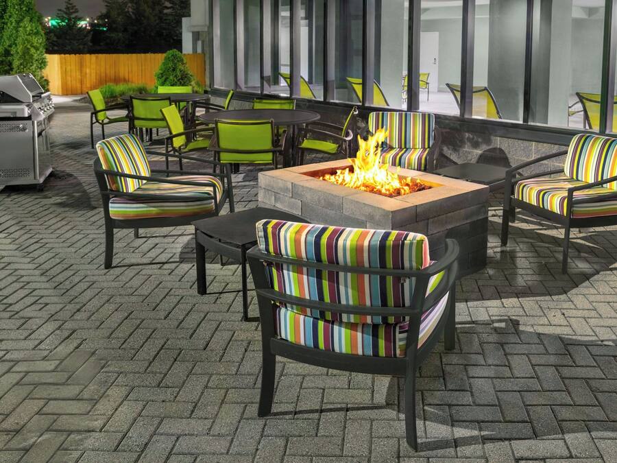 An outdoor patio area with a fire pit, green and striped chairs, and a grill.