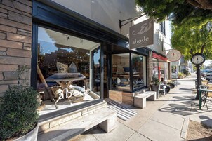 Vitrine com grandes janelas exibindo artigos de decoração, uma placa com o dizeres "abode" e área externa com mesas e cadeiras.