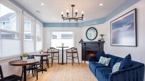 A living room with a blue sofa, a fireplace, a dining area with a table and chairs, and large windows. - BytheSea Inn  (Half Moon Bay)
