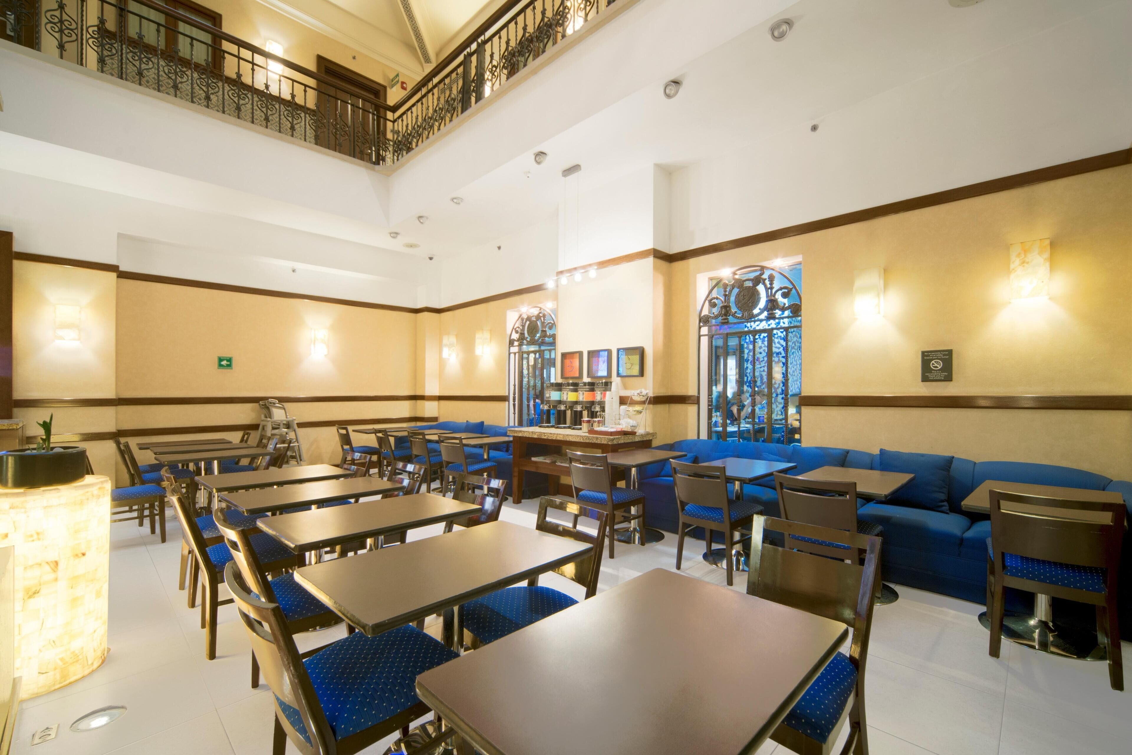 A hotel lobby with multiple seating areas, including tables and sofas, a staircase, and a large stained glass window.