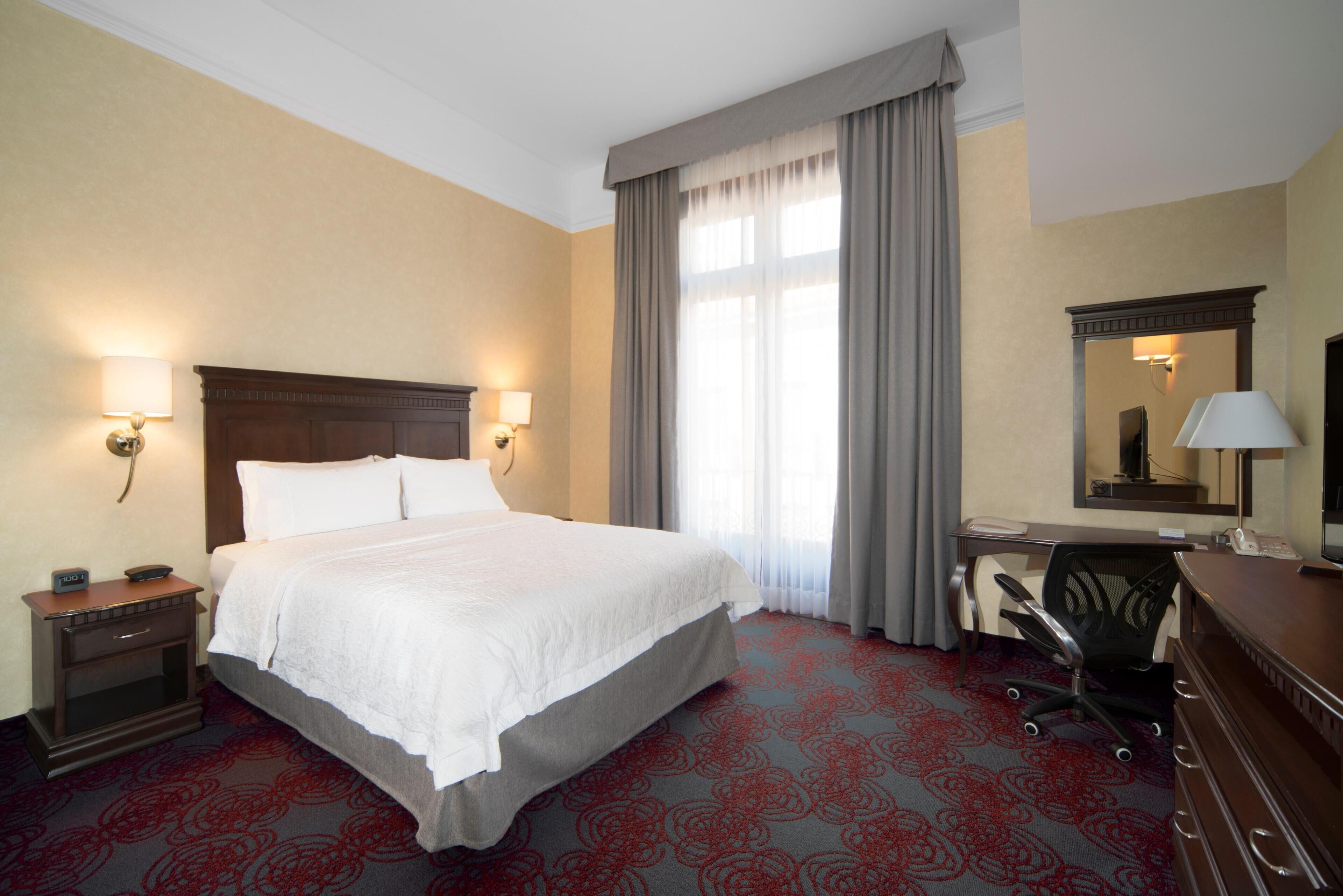 Une chambre d’hôtel avec un grand lit, des lampes de chevet, un bureau avec une chaise et un miroir.