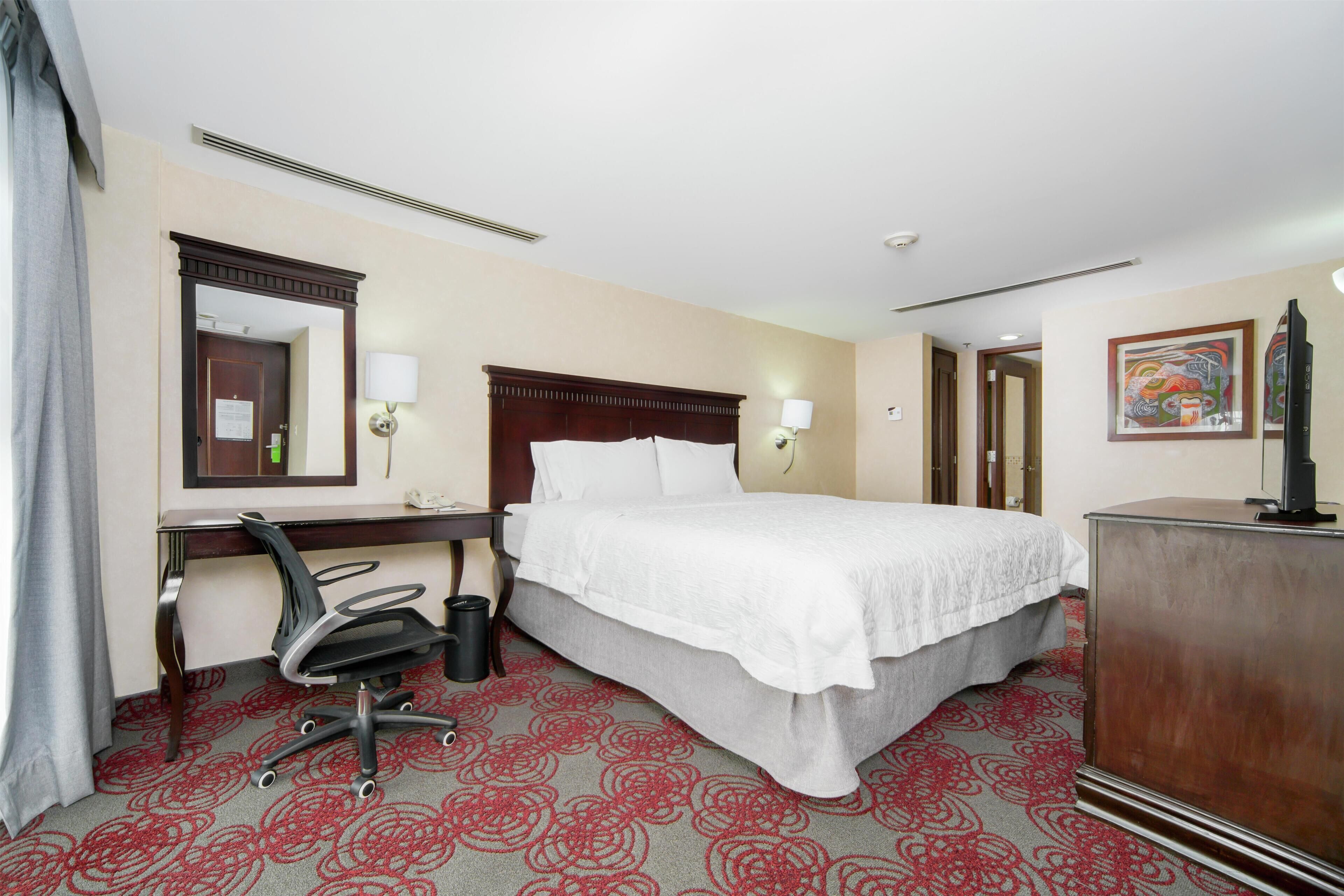 A hotel room with a bed, desk, chair, and a dresser.