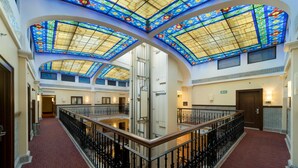 A hotel lobby with a red carpet, black wrought iron railings, and a glass ceiling with stained glass.