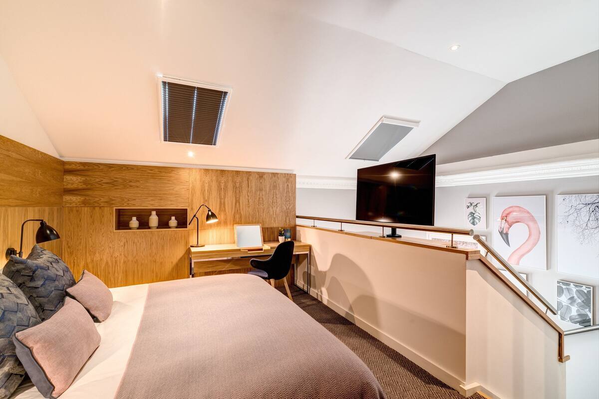 A hotel room with a bed, desk, chair, TV, artwork, and a window.