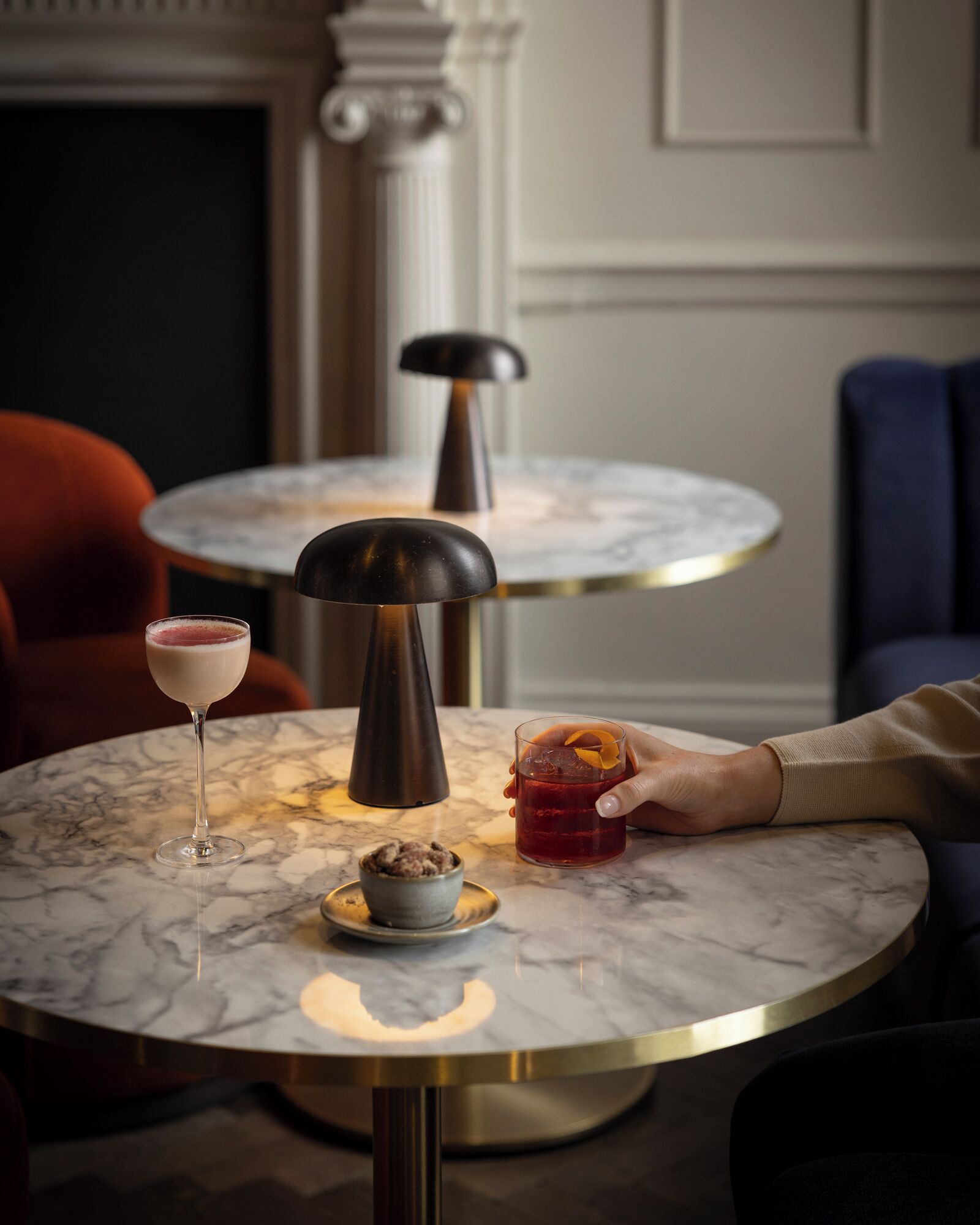 Ein Marmortisch mit einer Lampe, einem Glas roter Flüssigkeit und einer Nachspeise auf einem Teller.
