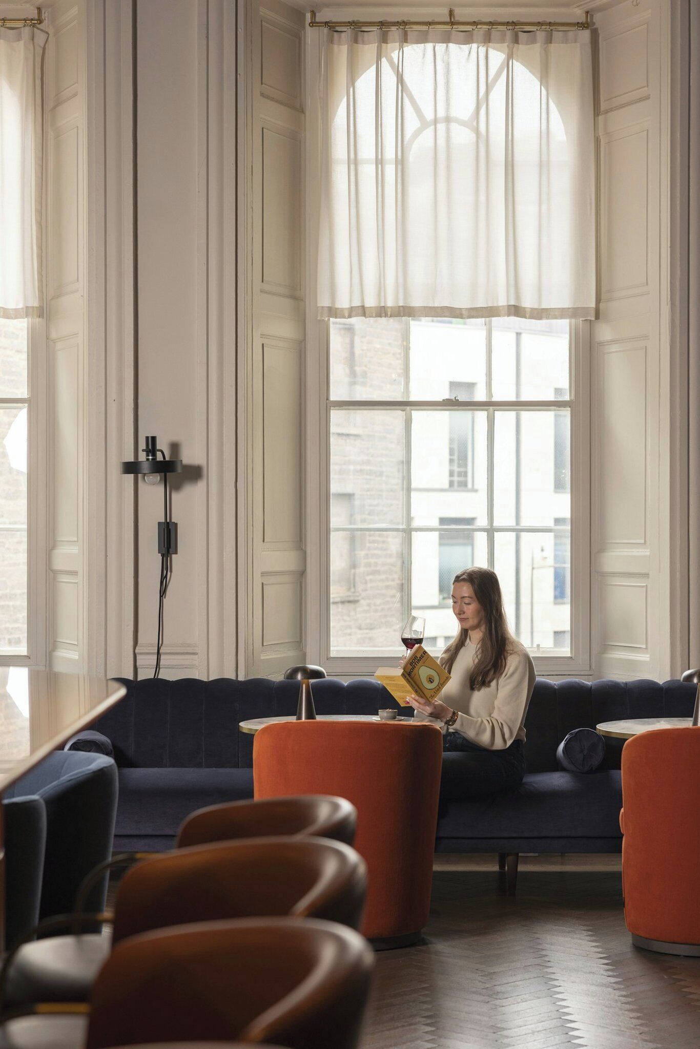 A room with a sofa, orange ottomans, and a person reading a book.
