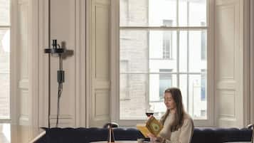 A room with a sofa, orange ottomans, and a person reading a book.