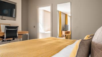 A hotel room with a bed, a desk, a chair, a television, and a large mirror.