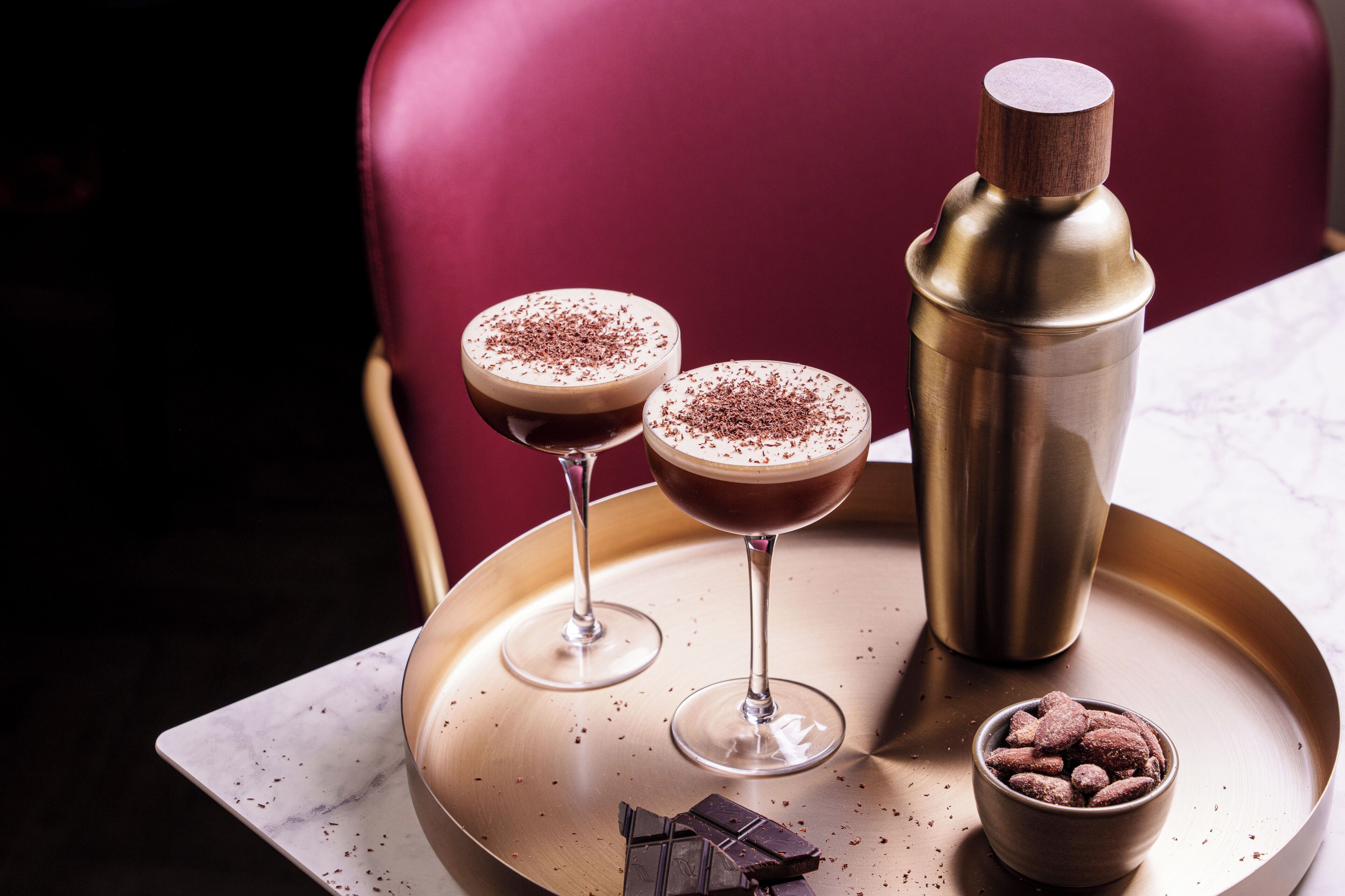 Two martini glasses with a frothy drink and a gold shaker on a tray.