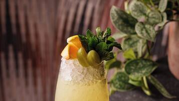 A cocktail glass with ice, garnished with mint, orange slice, and olives, placed on a dark surface.