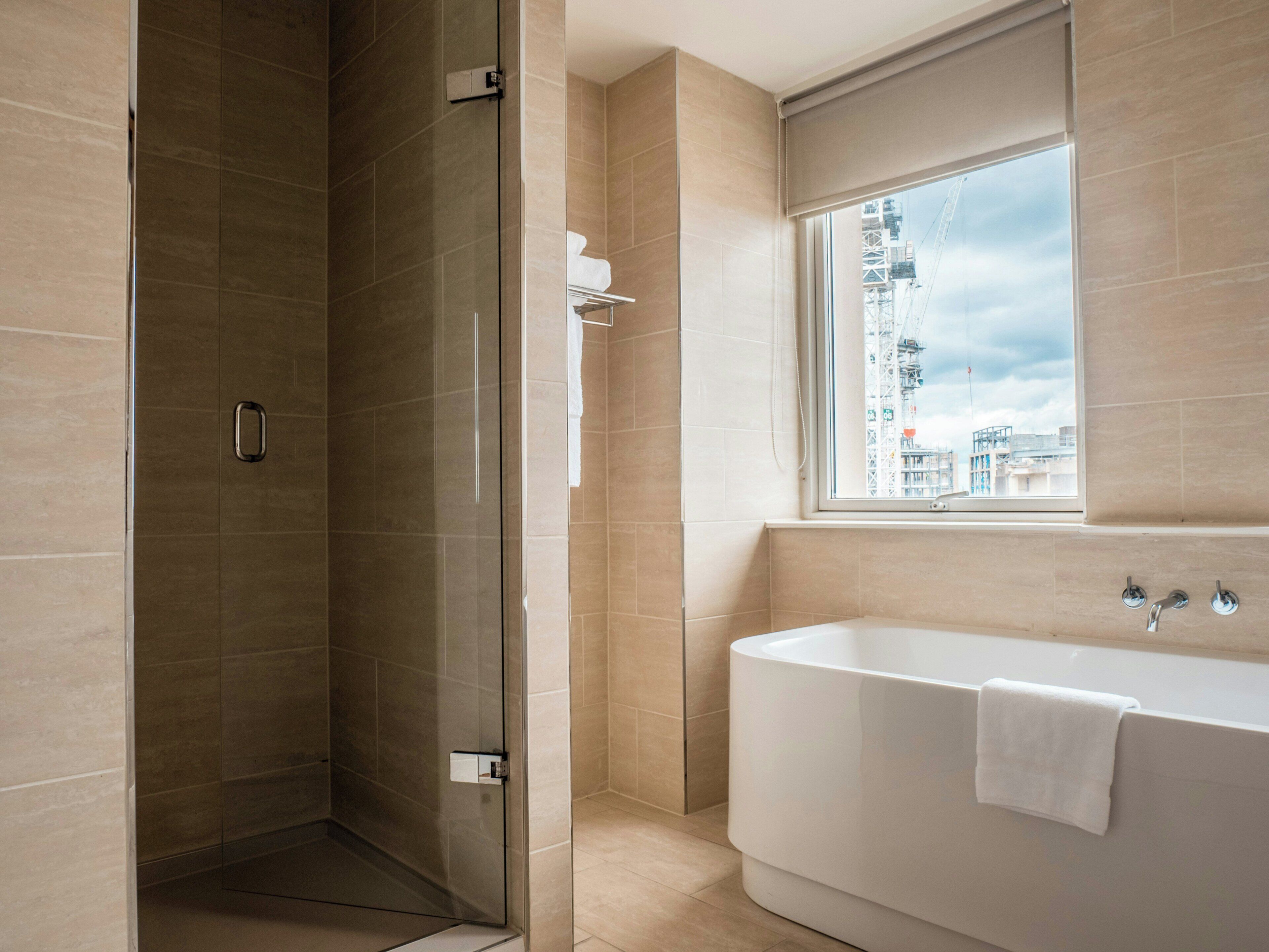 A modern bathroom with a glass-enclosed shower, a large bathtub, and a window with a city view.