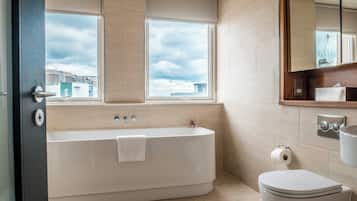 A modern bathroom with a bathtub, toilet, and large windows offering a view of the cityscape.