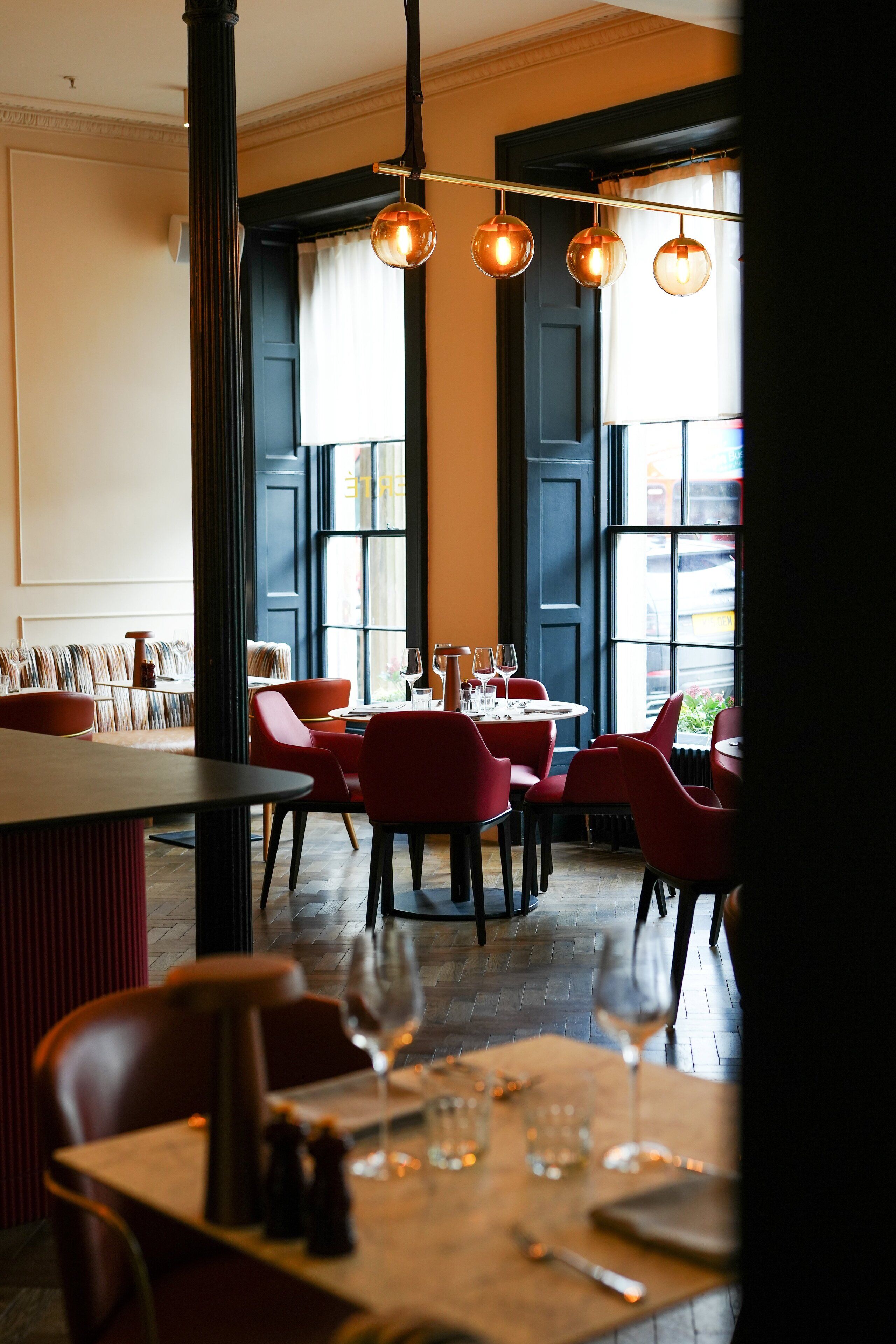 A restaurant interior with red chairs, wooden tables, and hanging spherical light fixtures.