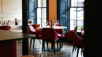 Interior de restaurante con sillas rojas, mesas de madera y lámparas esféricas colgantes.