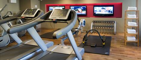 Un gimnasio con cintas de correr, bicicletas estáticas y un televisor montado en la pared.