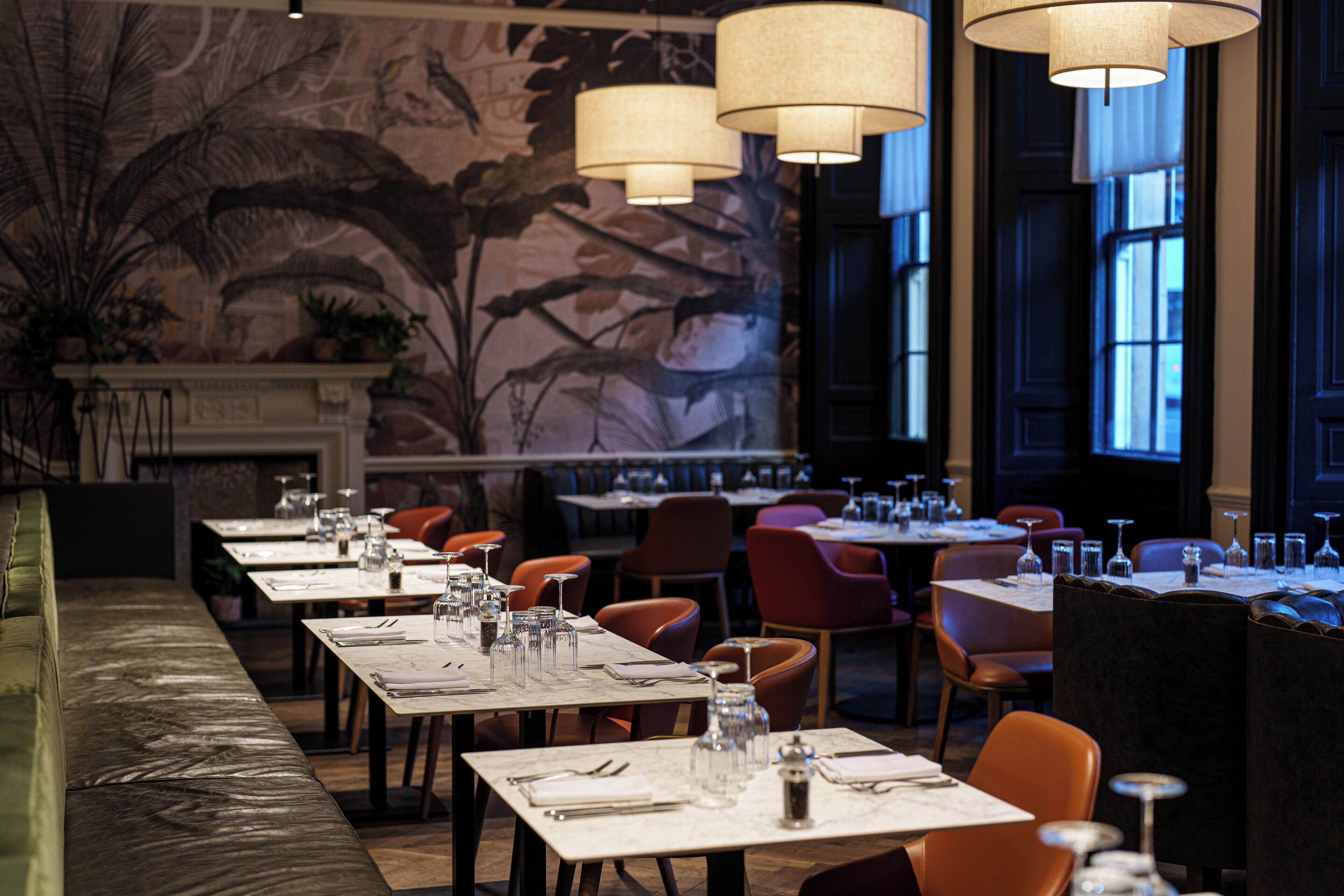 A restaurant with long tables, chairs, and hanging lamps.