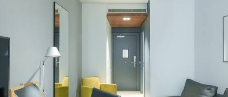 A modern hotel room with a desk, chair, sofa, and a mirror.