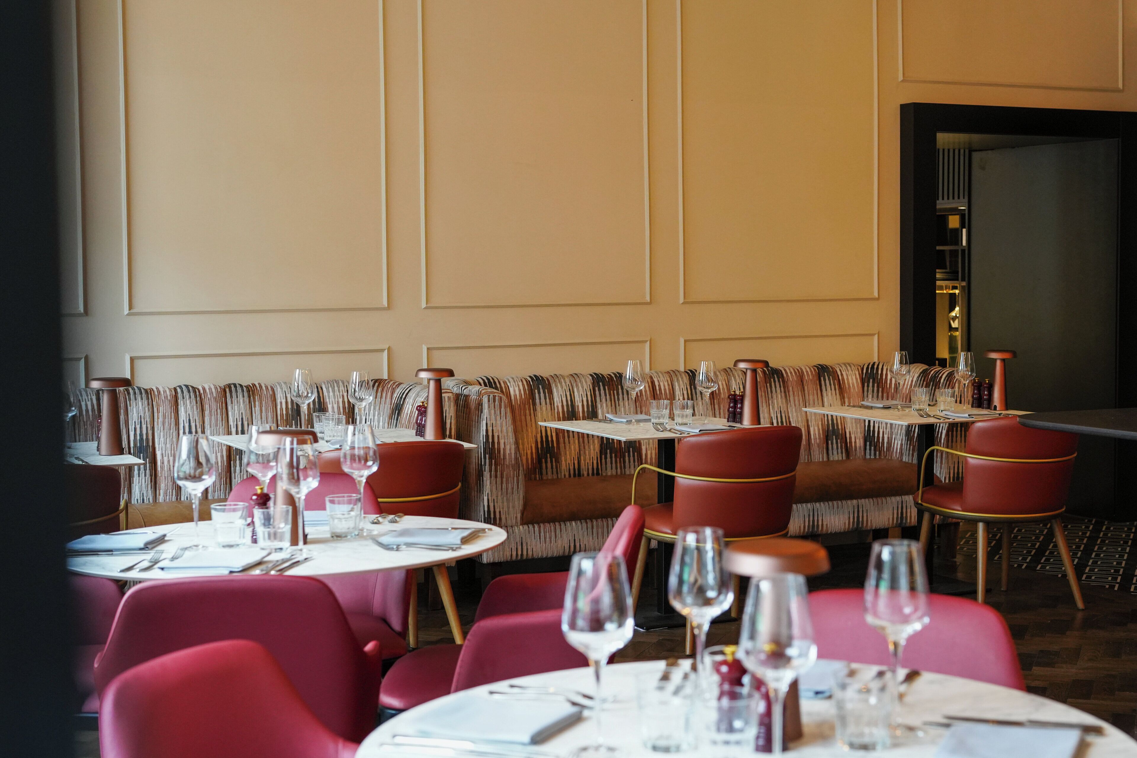 A restaurant with round tables and red chairs, featuring a patterned bench seating area.