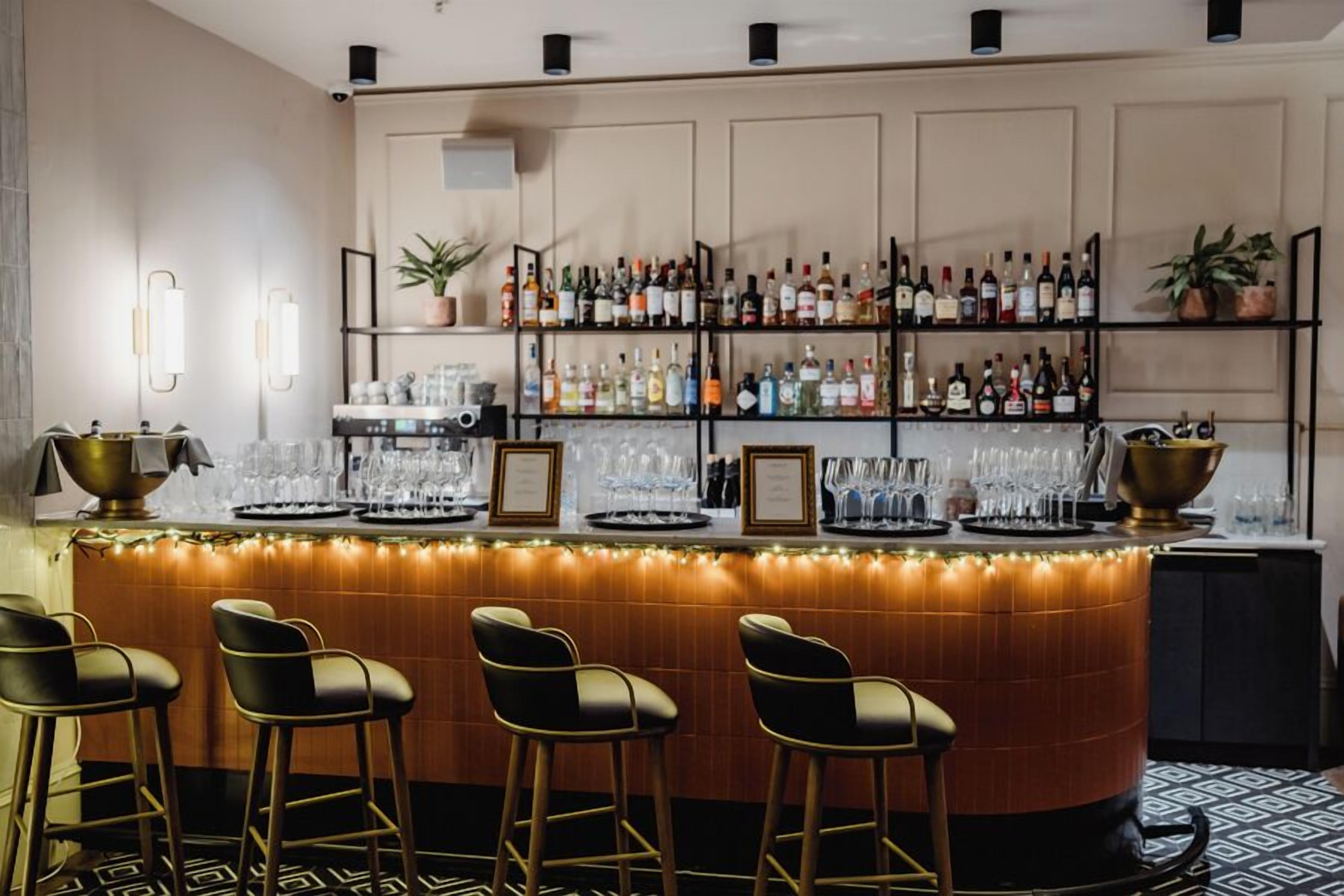 Una zona de bar con mostrador, varias estanterías llenas de botellas y taburetes.