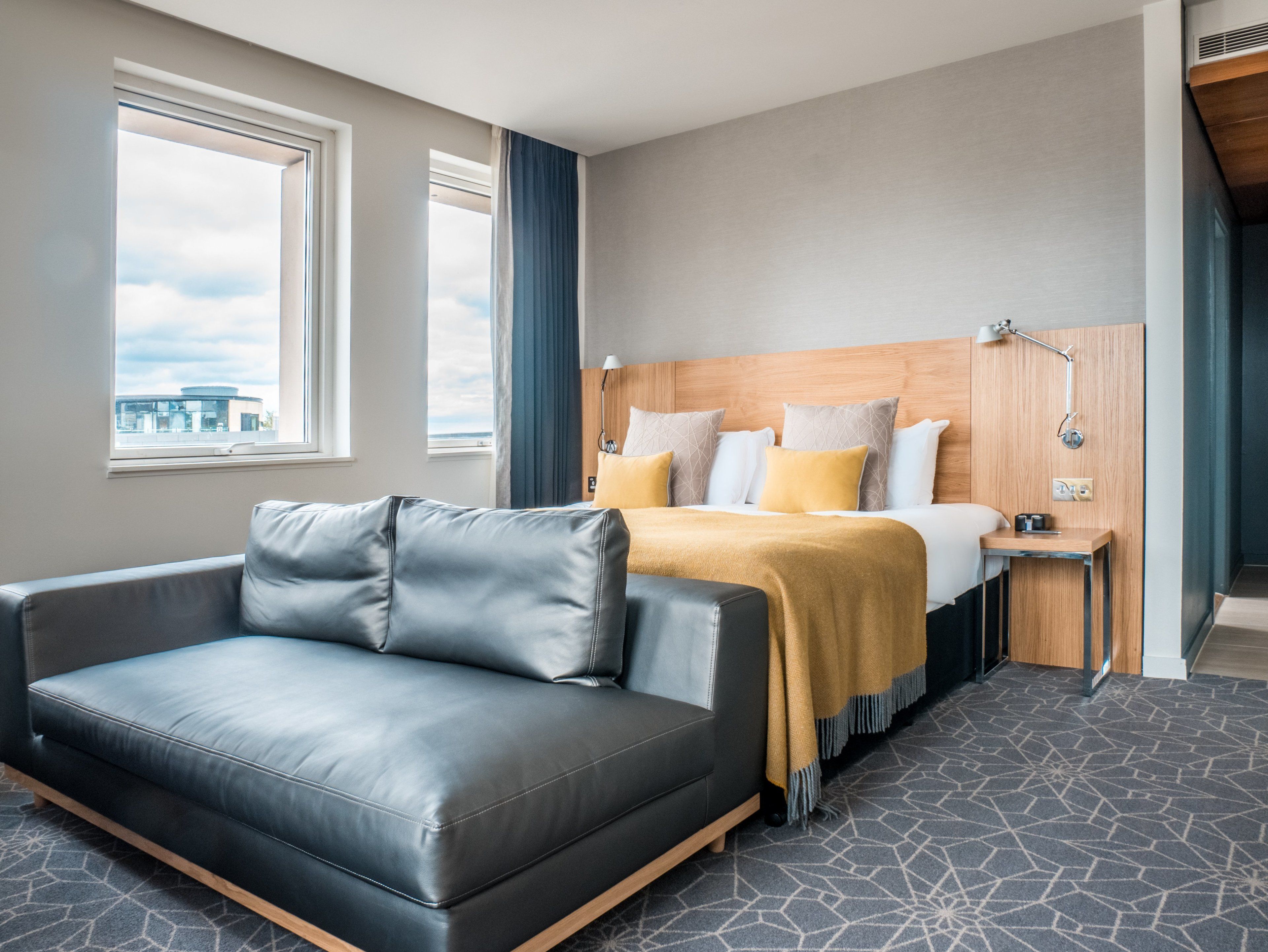 Una habitación de hotel moderna con cama, sofá, mesita de noche y vistas a la ciudad.
