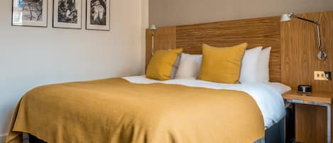 Una habitación de hotel con cama, mesita de noche y tres cuadros en la pared.