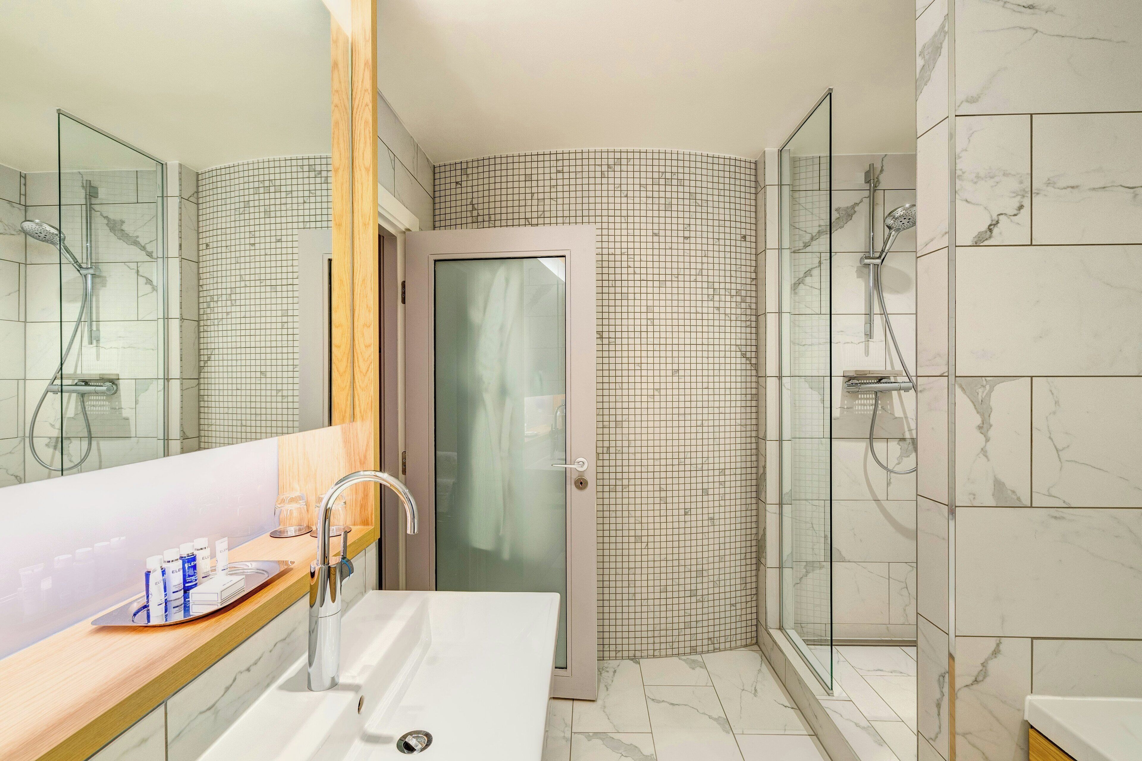 A modern bathroom with a glass shower enclosure, a wooden vanity, and a white sink.