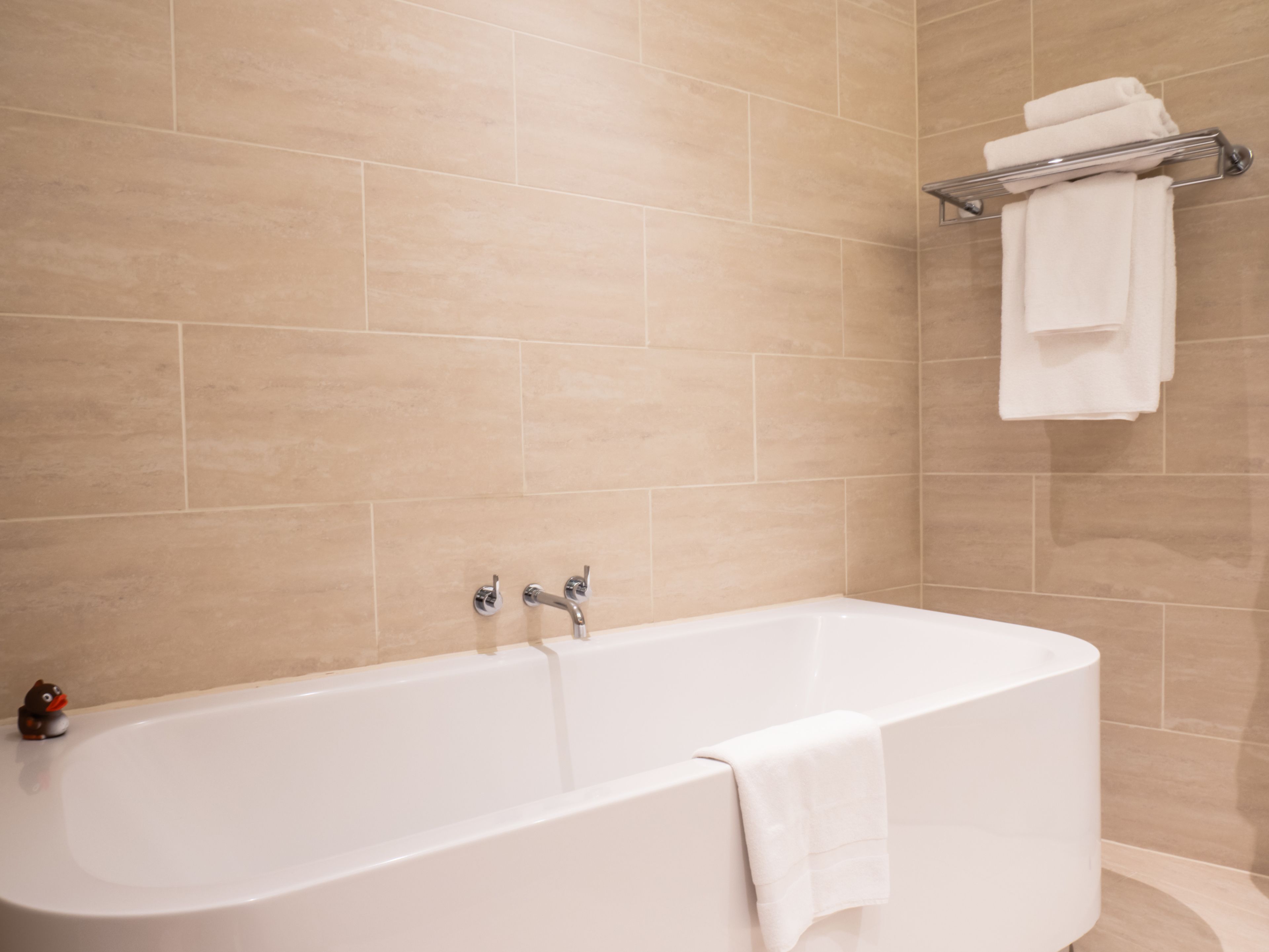Une salle de bain moderne avec une baignoire sur pieds, un porte-serviettes et une petite figurine de canard posée sur le sol.