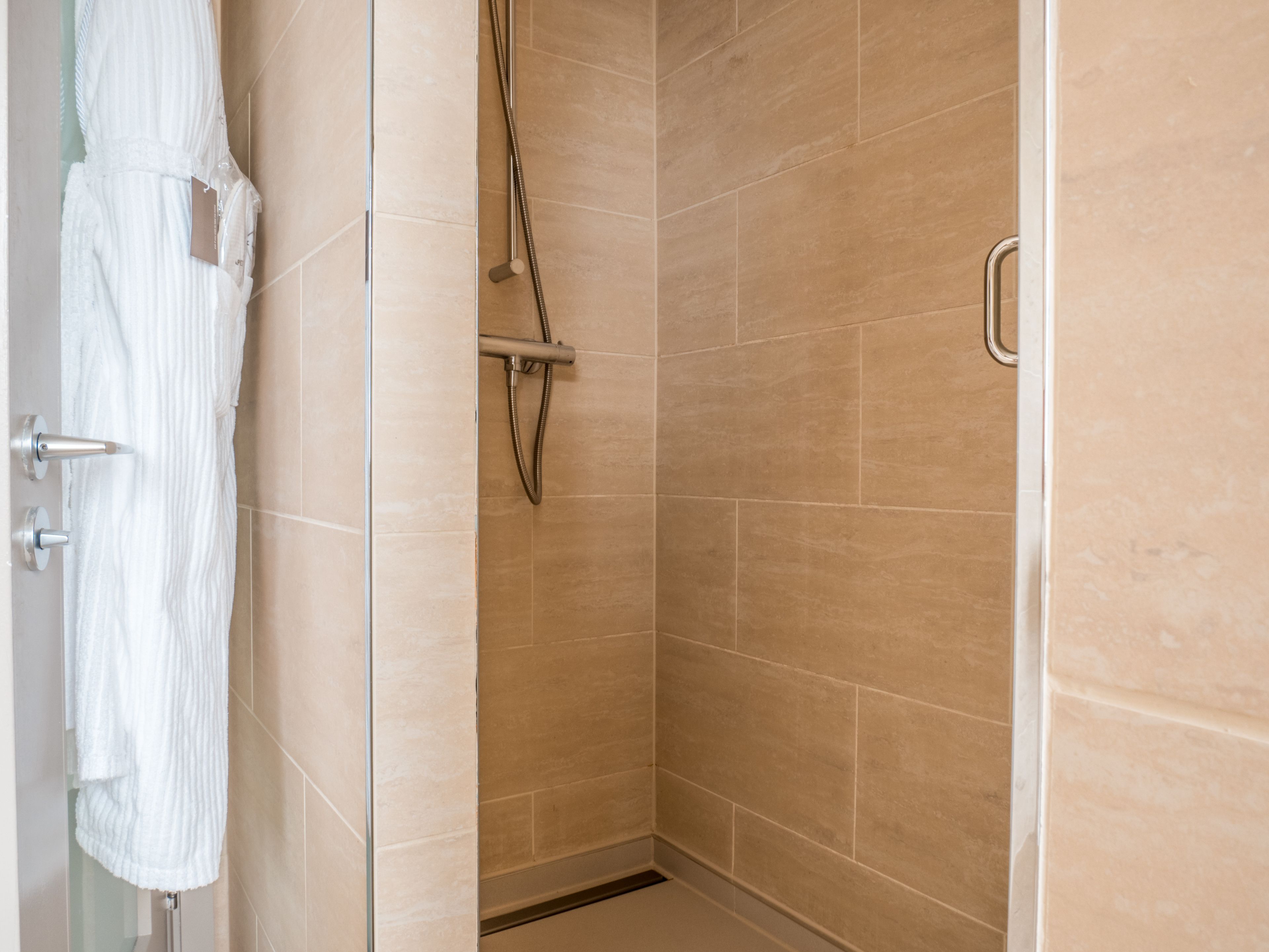 A walk-in shower with beige tiles, a glass door, and a towel rack.