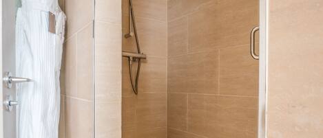 A walk-in shower with beige tiles, a glass door, and a towel rack.