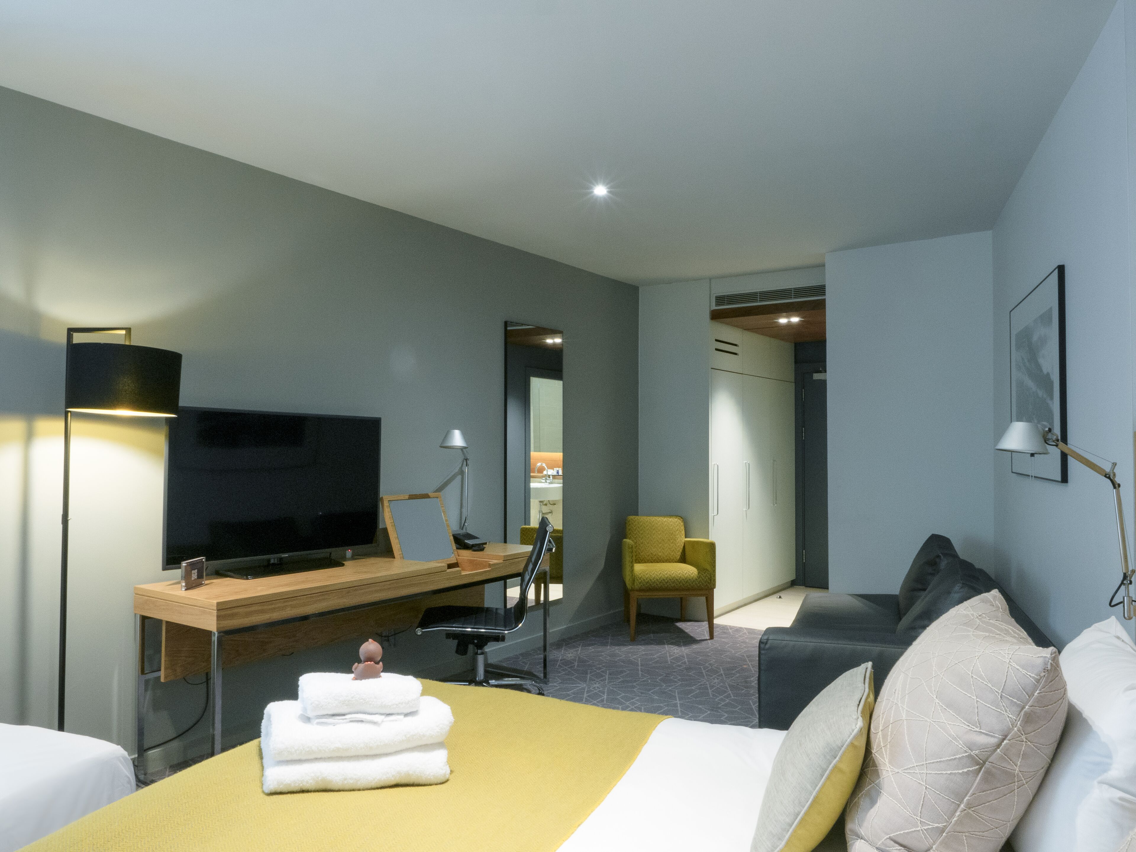 A modern hotel room with a bed, a desk, a TV, a chair, and a wardrobe.