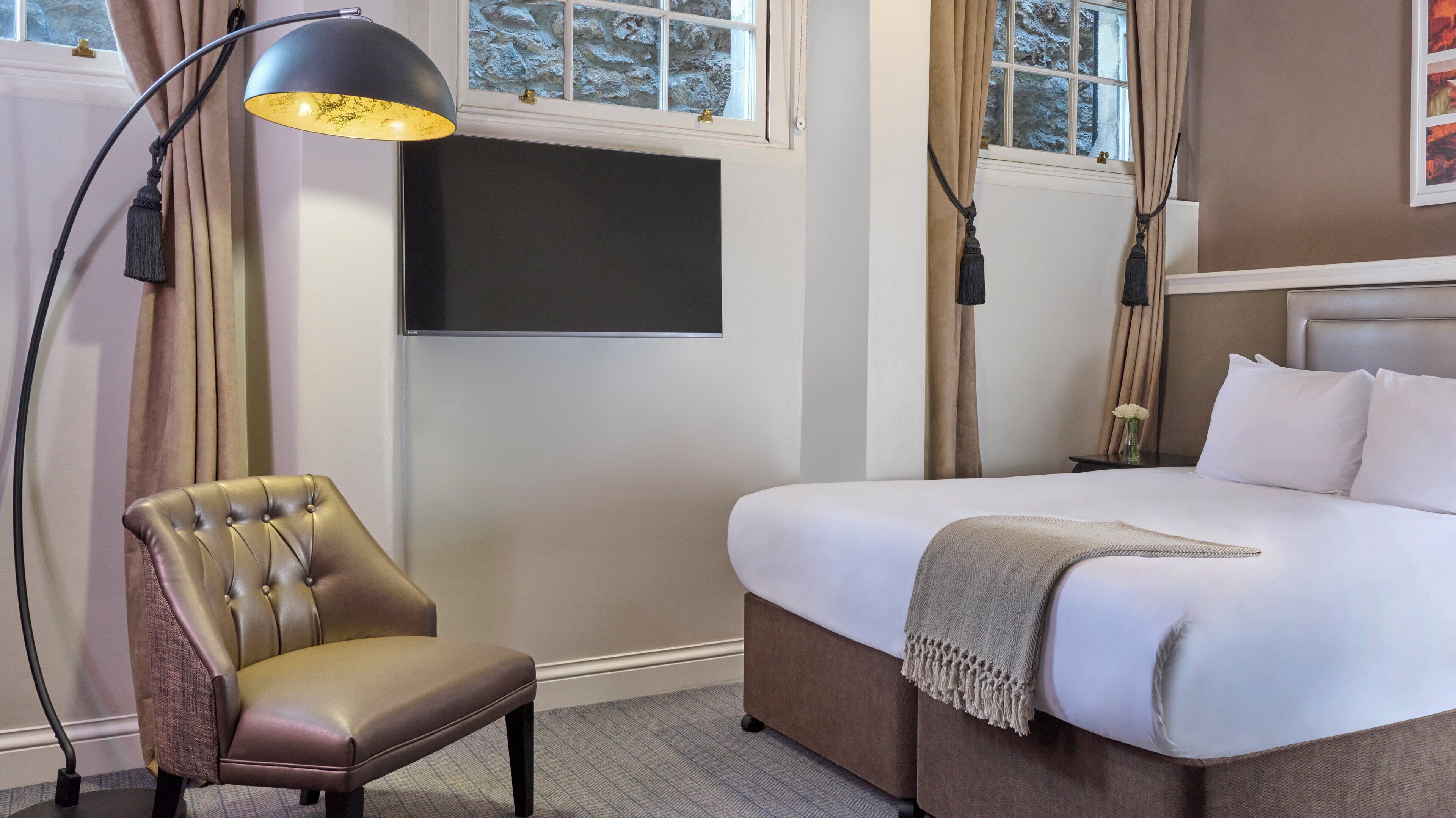 A hotel room with a bed, a chair, a TV, and a window with curtains.