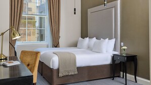 A hotel room with a large bed, a bedside table with a lamp, a chair, and a nightstand with a vase of flowers. - Fraser Suites Edinburgh (Edinburgh)