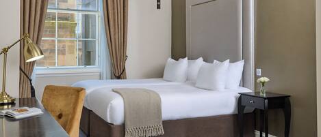 A hotel room with a large bed, a bedside table with a lamp, a chair, and a nightstand with a vase of flowers.