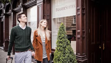 A man and a woman walking past a building with a sign that reads "FRASER SUITES".